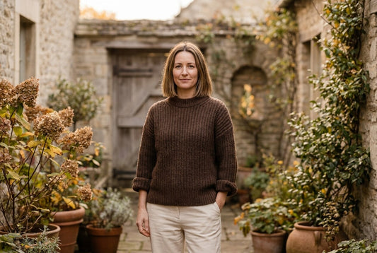Woman in a chocolate brown ribbed knit sweater standing in a stone courtyard