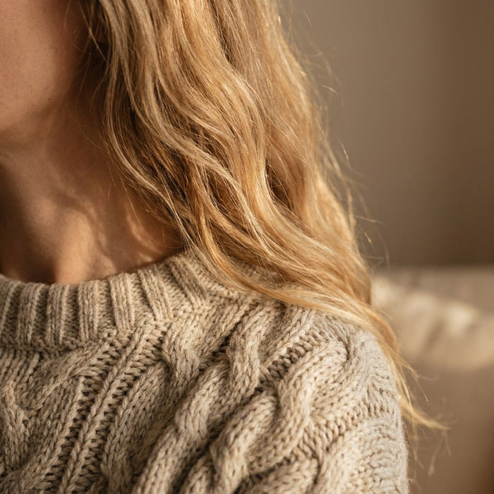 Blonde hair falling over the shoulder of an oatmeal cable-knit sweater in warm light