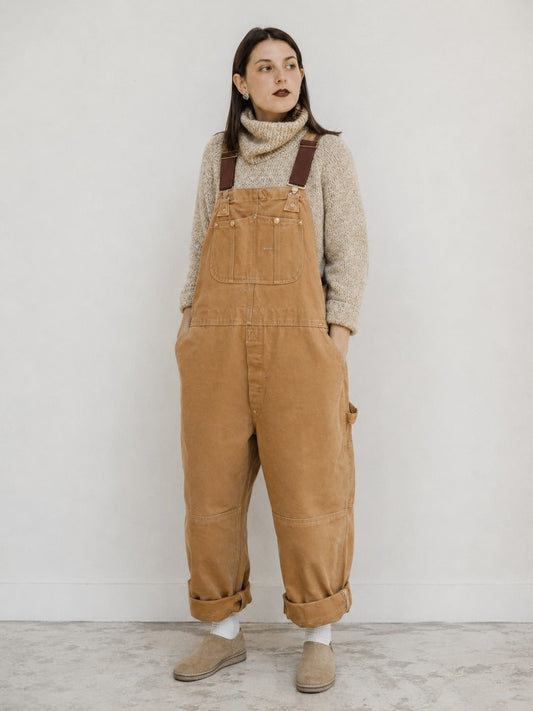 Beige canvas bib overalls worn with a knit turtleneck, front view 1